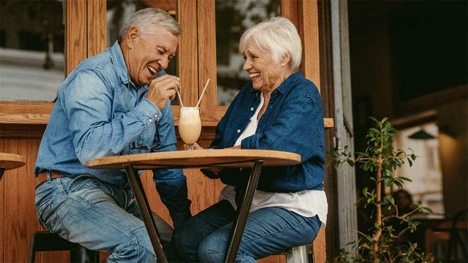 Pareja de ancianos sentados fuera de un restaurante riendo y disfrutando de una bebida fría