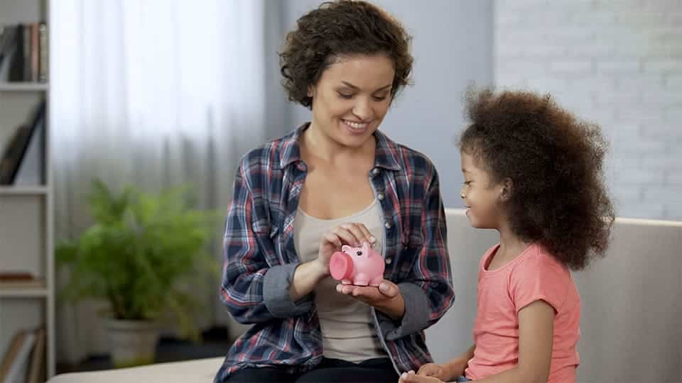 Madre e hija sentadas en el sofá echando monedas en una hucha