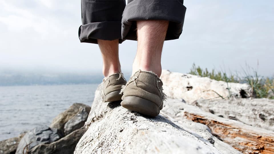 Persona en equilibrio sobre las rocas con un pie detrás del otro con el océano en la distancia