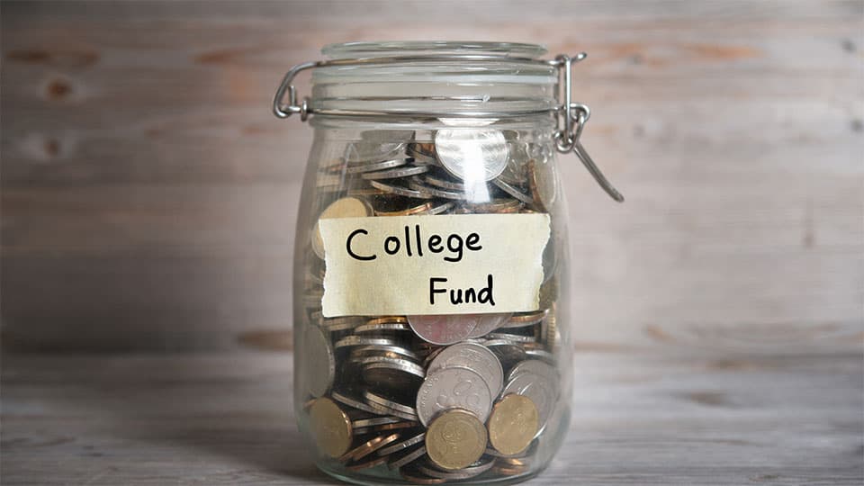 Jar of coins in mason jar with "College Fund" labeled on front resting on table