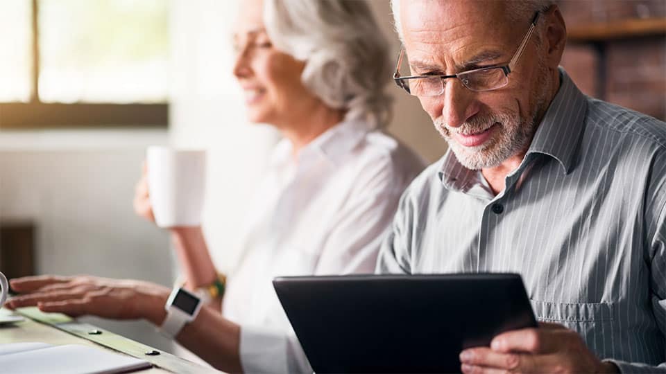 Pareja de ancianos sentados uno al lado del otro tomando café y mirando la pantalla de una tablet