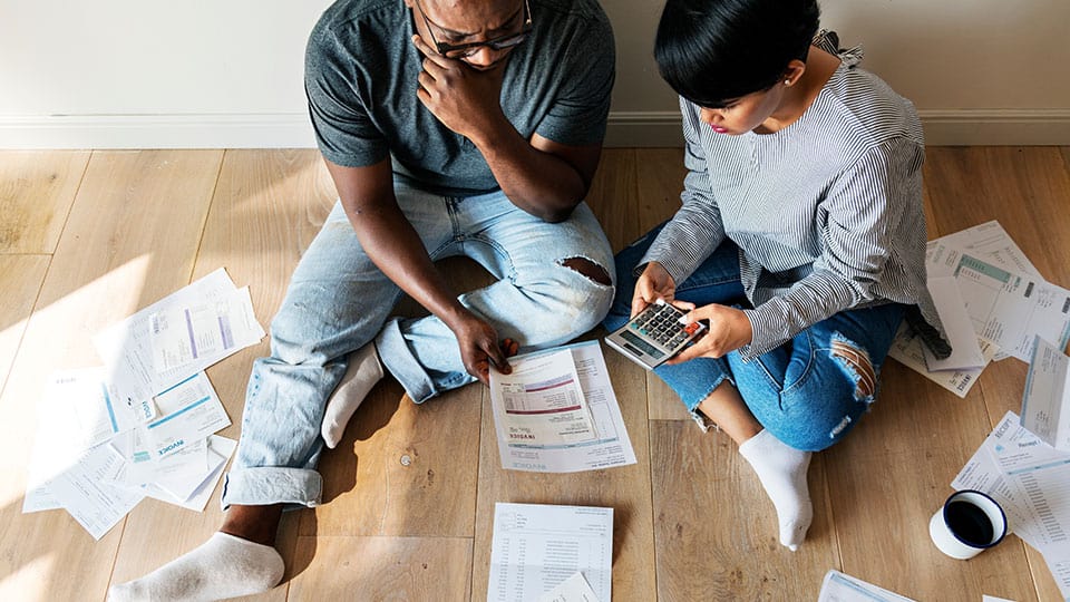 Couple sitting on wooden floor calculating bills with paperwork and calculator