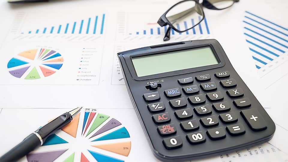 Charts printed on paper resting on flat surface with glasses, a calculator and pen sitting on top of them