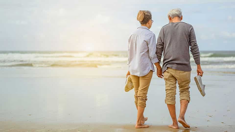 Older couple walking and holding hands on beach