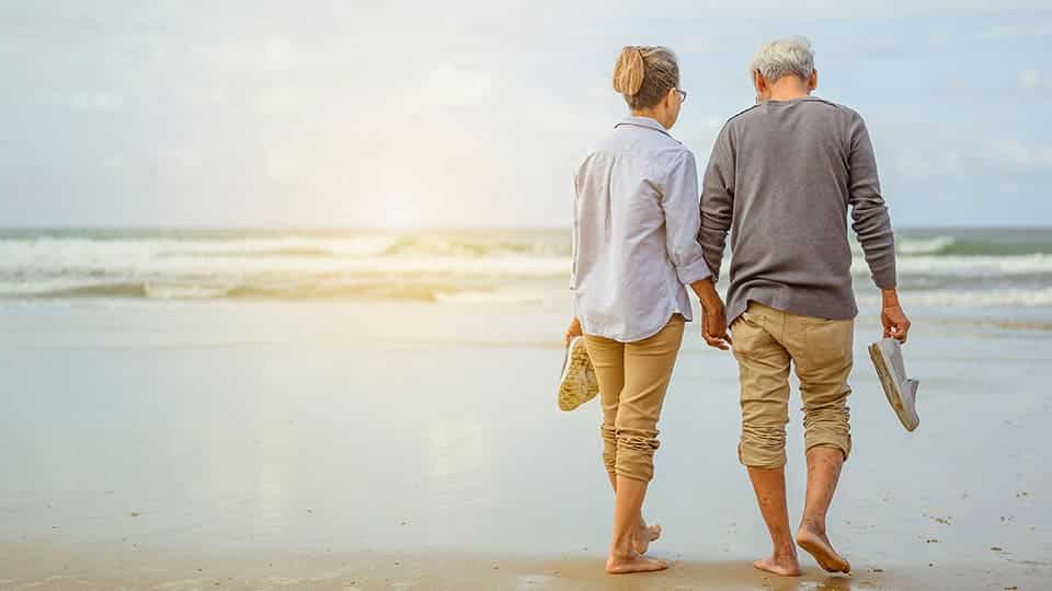 Pareja de ancianos caminando y cogidos de la mano en la playa