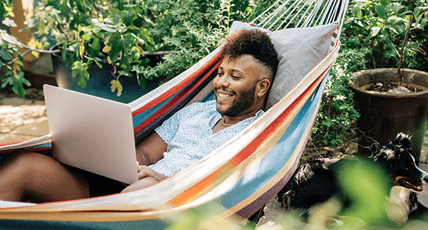 Happy guy sitting in hammock using laptop