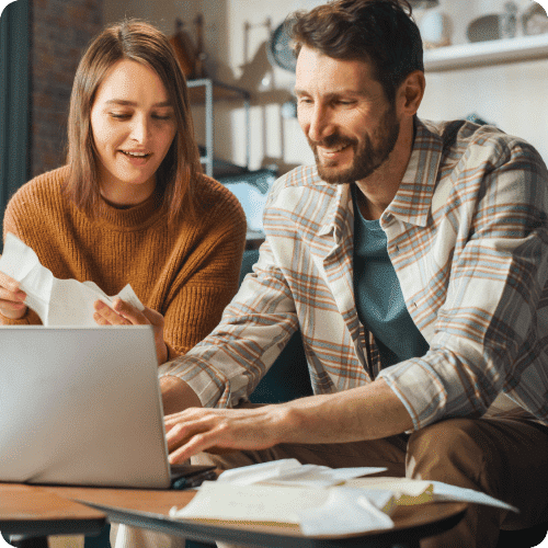 Man and woman sitting side by side on couch using computer and looking at documents