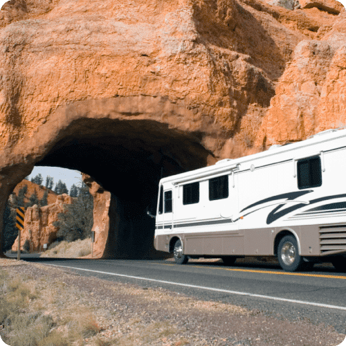 RV traveling under bridge formed by red rock