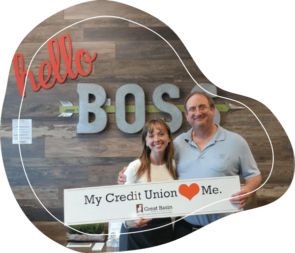 Male and female with arms around one another standing in front of "Hello Boss" sign and holding sign that says "My Credit Union Loves Me"