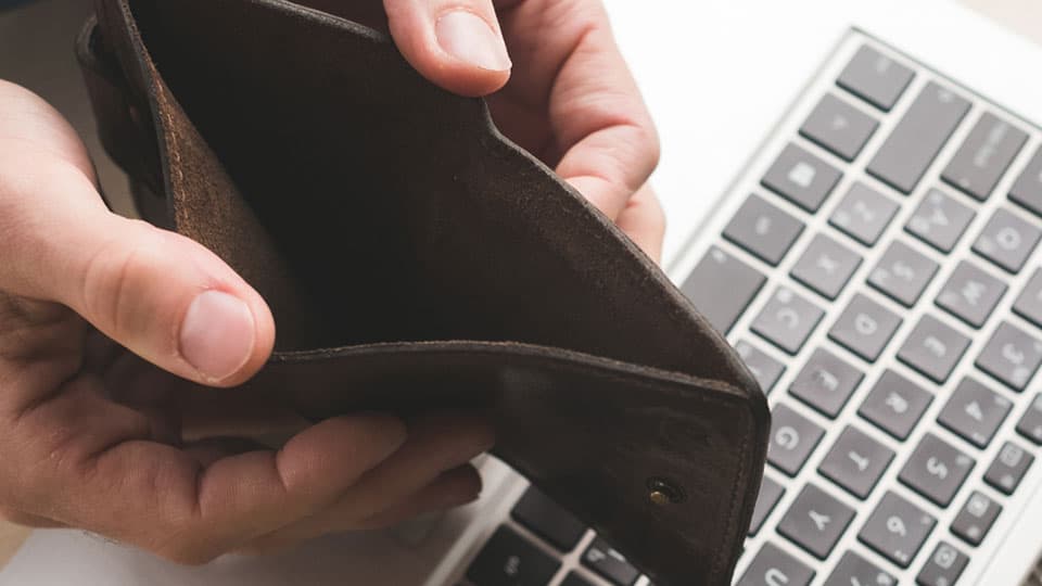 Hombre abriendo una cartera vacía con ambas manos sobre el teclado de un portátil