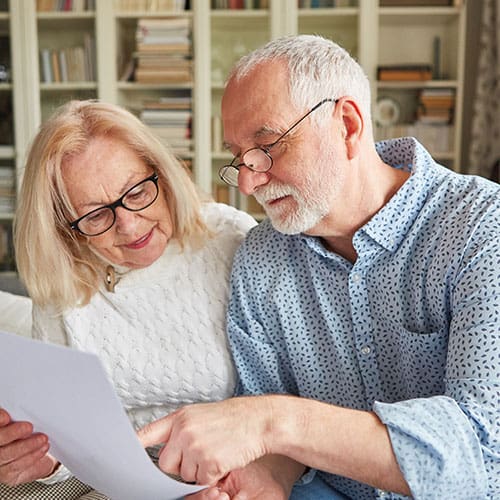 Male and female couple sitting closely together reviewing a document in office of home