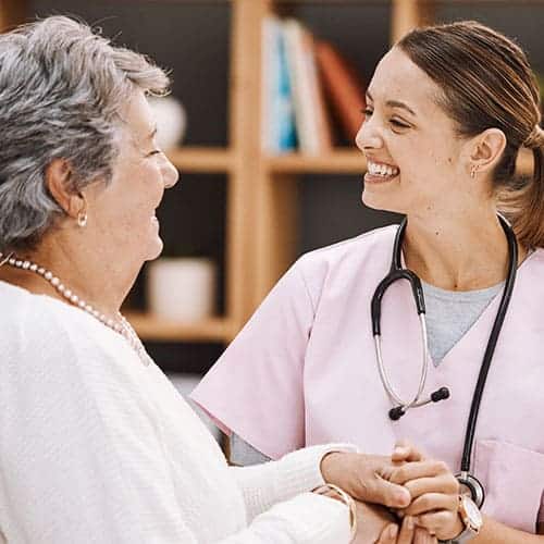 Female doctor smiling and holding hands with female patient