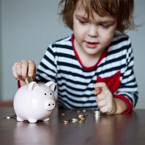 Little girl placing coins in piggy bank