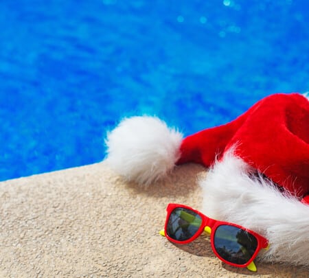 Red santa hat and red sunglasses resting on surface next to pool