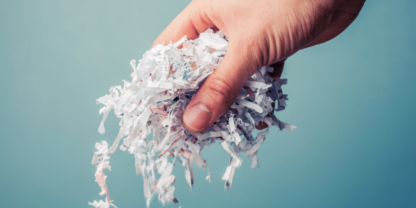 hand holding shredded papers isolated on a baby blue background