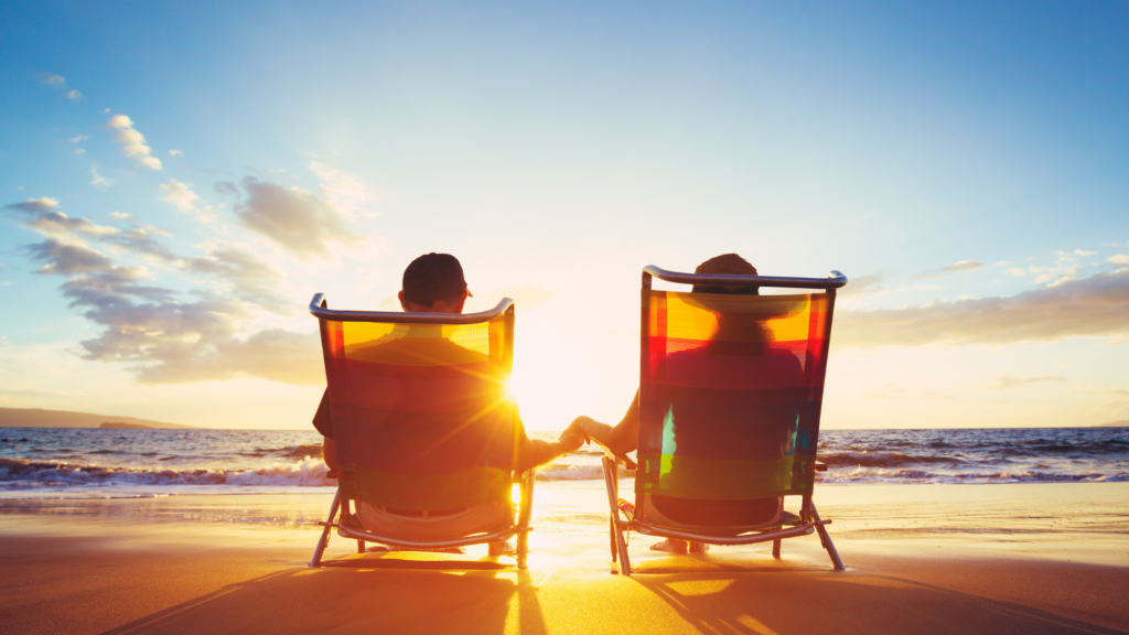 couple sitting on the beach at sunset in beach chairs.