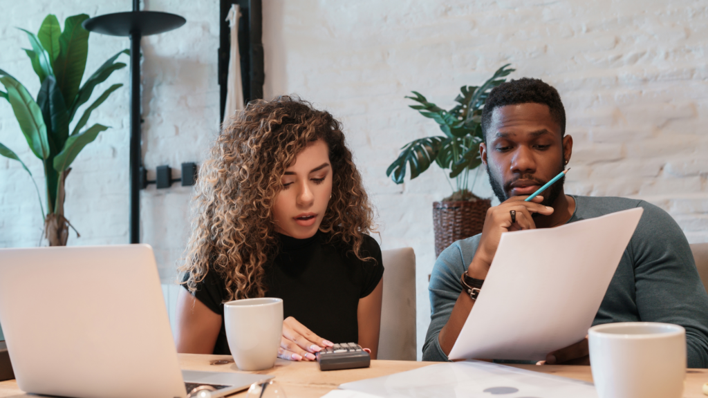 couple sitting in a kitchen reviewing finances with a laptop and paperwork