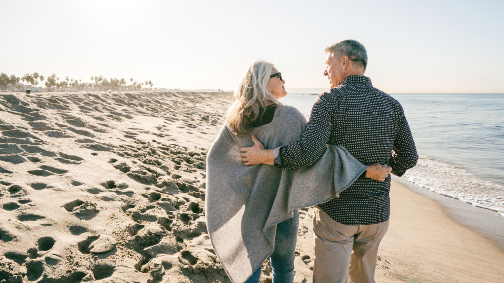 pareja de jubilados caminando del brazo por la playa.