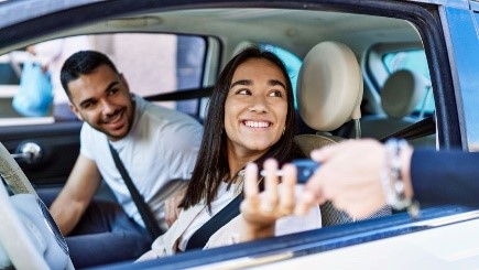 Young Hispanic couple in a car getting keys handed to them.