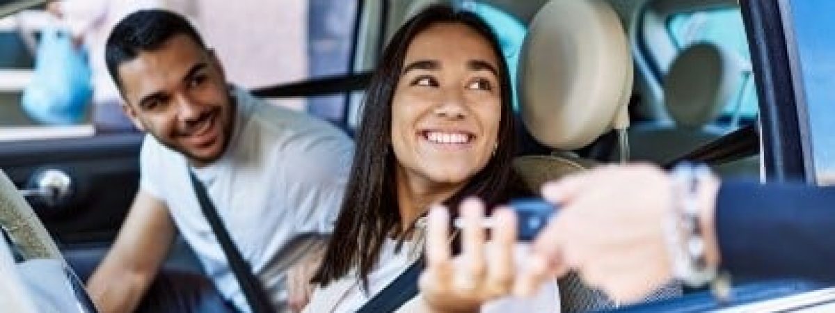 Young Hispanic couple in a car getting keys handed to them.