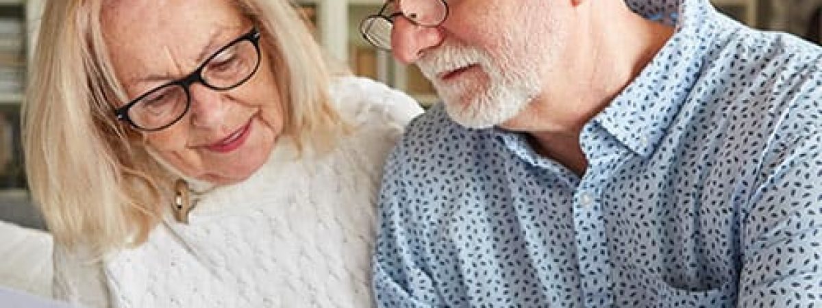 Male and female couple sitting closely together reviewing a document in office of home